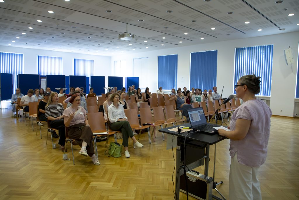 Foto: Stuhlreihen mit Publikum, Rednerin am Pult